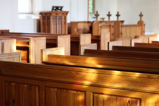 Rows of traditional wooden church pews illuminated by sunlight