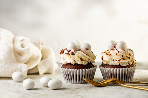 Stock photo showing a close-up view of a batch of freshly baked, homemade, chocolate cupcakes in paper cake cases, one unwrapped cake with missing bite. The cup cakes have been decorated with swirls of chocolate piped icing and chocolate pieces.