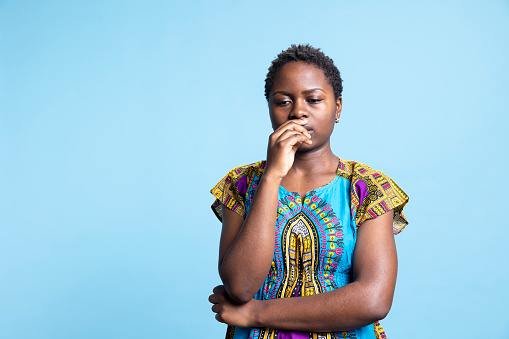 Contemplative young woman appears cautious in front of the camera, considering issue before coming to a decision. African American girl in studio contemplating and is uncomfortable.