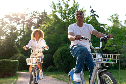 african-american couple rides bicycles in the park and talks, man and woman walk on eco-transport communicate and laugh in nature in summer