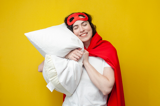 cute young girl in superman costume sleeps on soft pillow and rests, the concept of healthy sleep, woman superhero wants to sleep