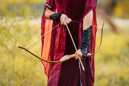 Young magical woman preparing to fire an arrow with her bow in the forest. Close-up.