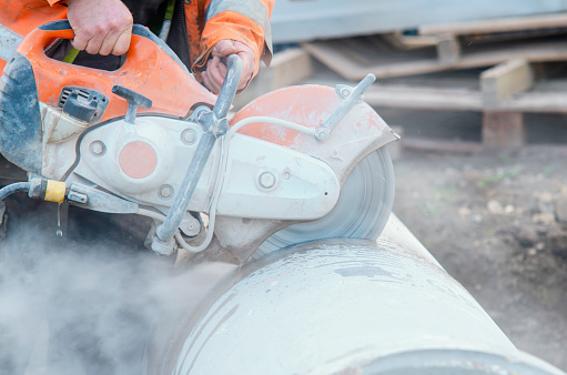 Construction worker cutting concrete pipe for drainage using a cut-off saw. Cutting concrete with a diamond blade creating cloud of silica dust