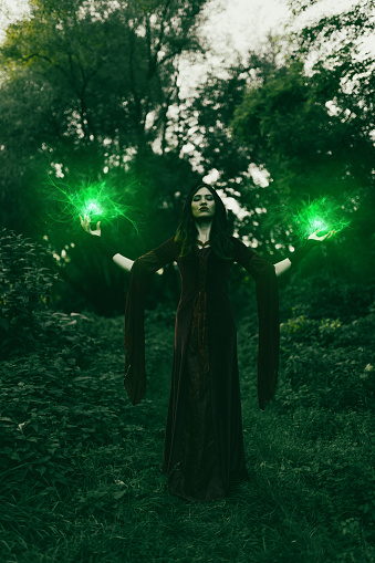 Young woman dressed like an evil witch and practicing magic in the forest.