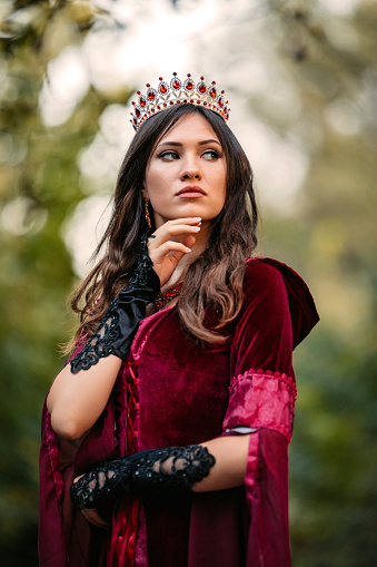 Young woman dressed like an evil queen standing in the forest.
