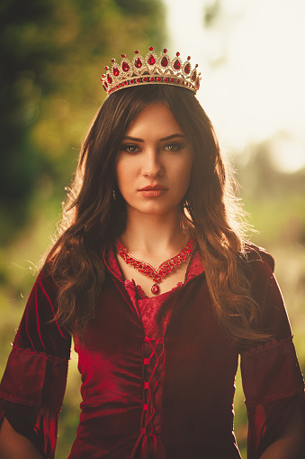 Portrait of a young woman dressed like an evil queen standing in the forest.