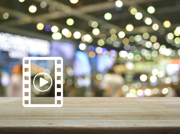 Play button with movie icon on wooden table over blur light and shadow of shopping mall, Business cinema online concept