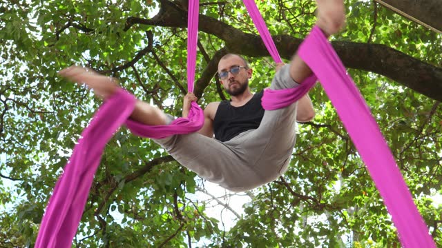 Young man practicing aerial silk exercises at the public park