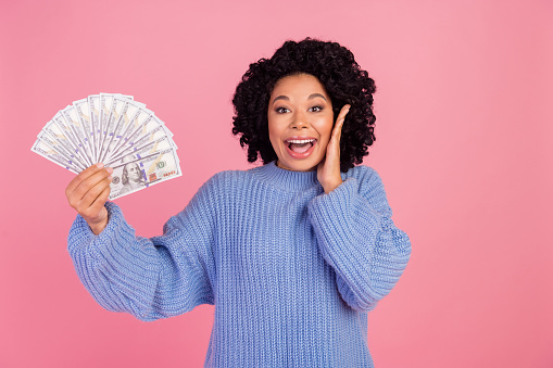 Photo of impressed funky woman wear blue pullover rising dollars fan arm cheek isolated pink color background.