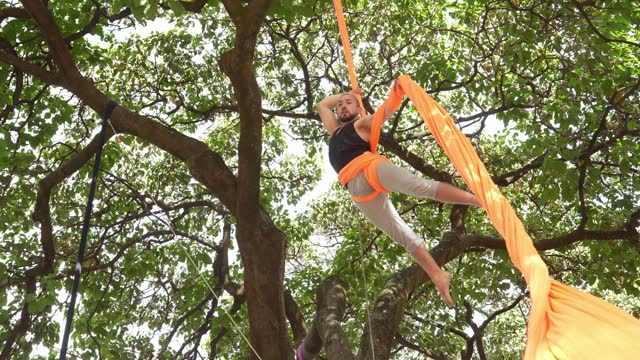 Young man practicing aerial silk exercises at the public park