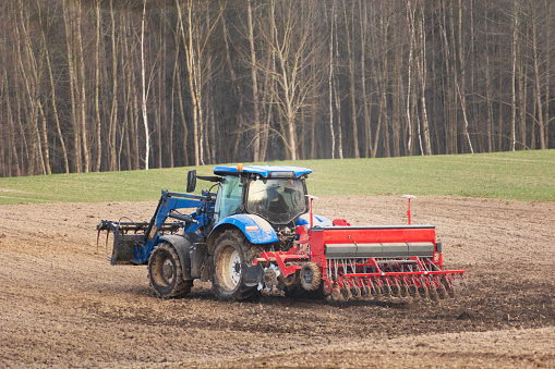 Agricultural tractor with seeder in the field, spring day, eastern Poland