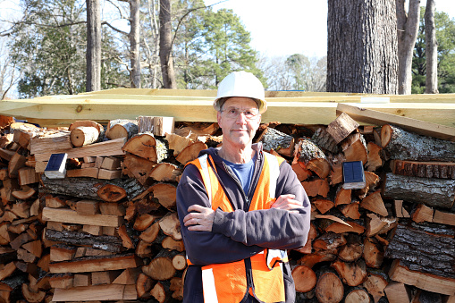 Man who works for a arborist stands in front of his stacks of wood.