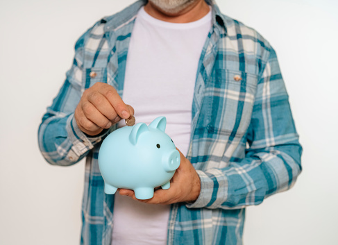 man in a casual shirt saving money for a rainy day in the piggy bank, investment, saving money, currency, deposit. Indoor studio shot isolated on a white background