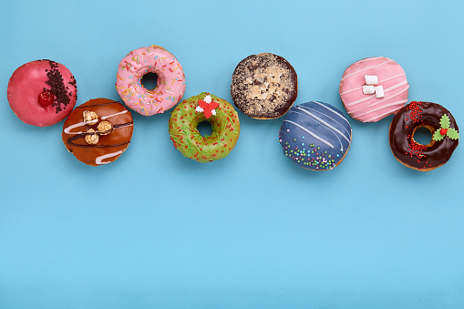 Sweet colored donuts on a blue background, laid out in the form of various geomitric figure, arrow, square, line, triangle, top view. Desserts, game of colors, blue background