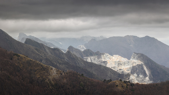 Among the clouds and the rocks, the marble quarries of Carrara exude an eerie charm. On this ominous day, where stormy clouds dance overhead, the rugged beauty of the marble emerges in stark contrast. A landscape shaped by centuries of excavation tells a story of art and industry, while the threatening sky adds a touch of drama. Nature and human endeavor collide, creating a scene that captures both the harshness and haunting allure of Carrara's marble quarries