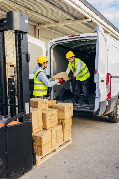 istock Two warehouse workers transfer cardboard boxes from a forklift to a delivery van 2042829050