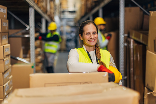 Portrait of a cheerful female warehouse manager holding a work helmet in her hands and looking directly at the camera