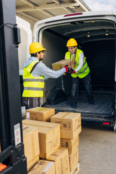 istock Two warehouse workers in reflective uniforms and hard hats are transferring cardboard boxes from a forklift to a delivery van, they are preparing packages for dispatch 2042849296