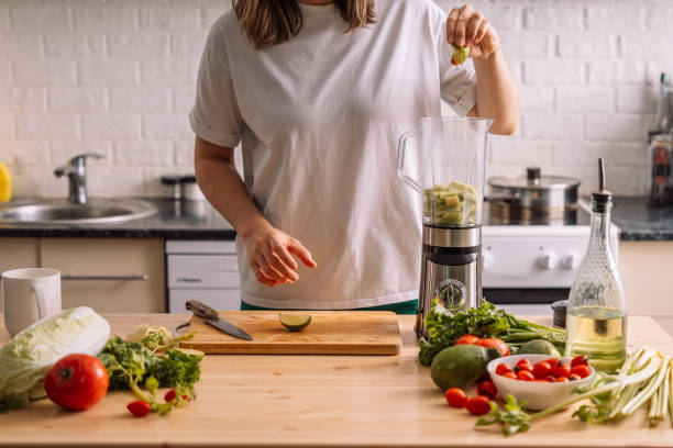 istock Lady in the kitchen presses a lime into a blender on a wooden table on which there are fresh vegetables 2042853656