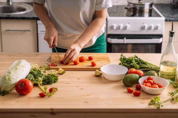 istock Lady slicing cherry tomatoes on a wooden table in front of the kitchen 2042853670