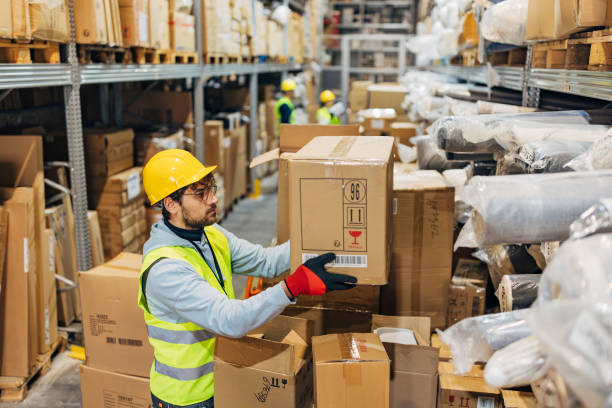istock Side view of a warehouse worker removing cardboard boxes from a shelf in a warehouse and placing them on a hand truck 2042855813