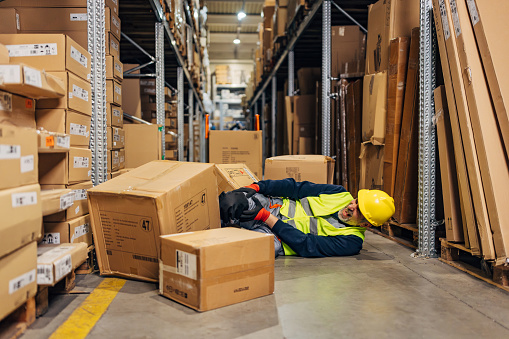 Cardboard boxes fell and knocked down a worker in the wholesale warehouse, he has a painful facial expression