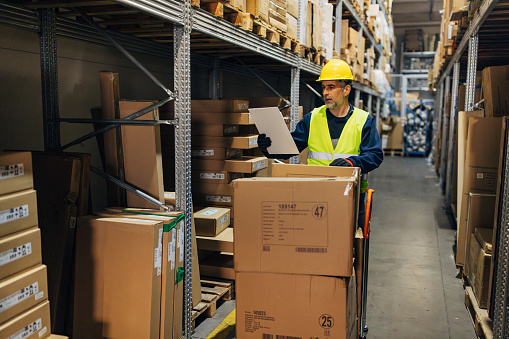 Warehouseman with clipboard checking delivery, stock in warehouse. Warehouse worker preparing products for shipment