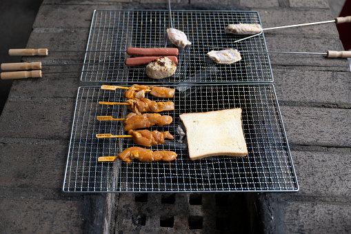 Meat skewers, chicken wings, and bread on outdoor barbecue grills