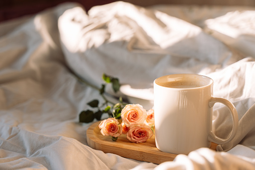 Glass of coffee with flowers on a wooden tray on a white bed.