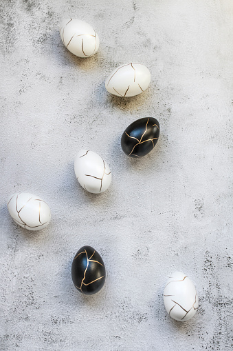 Vertical Easter background with luxury and elegant Easter black and white eggs decorated with gold on concrete background. Top view, flat lay. Happy Easter concept