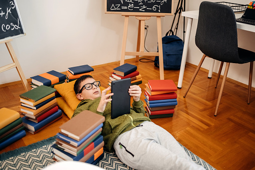 Boy working on school project at home while lying on back