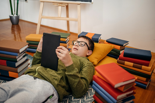 Boy working on school project at home while lying on back