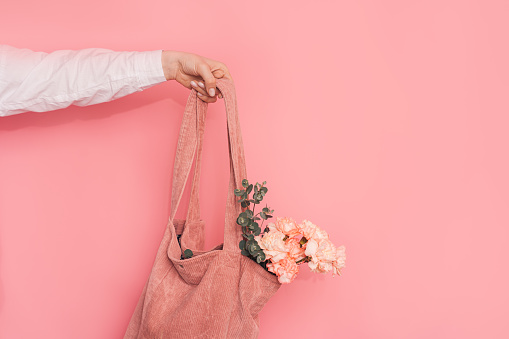 A hand holding a fabric dryer from which a bouquet of carnations and eucalyptus protrude against a pink background.