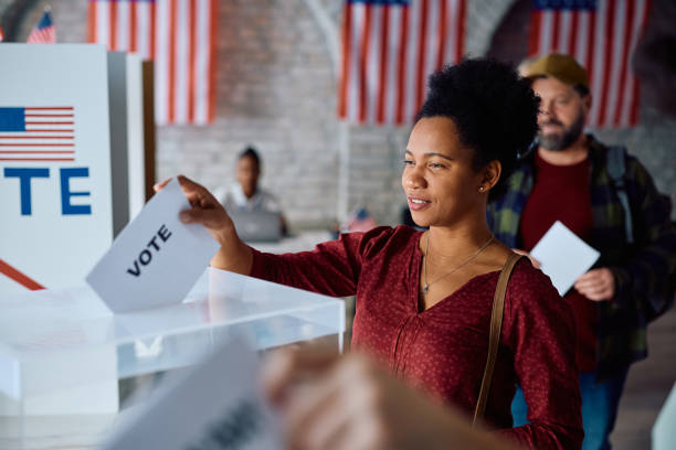 istock Black woman inserting her ballot into a box while voting during US elections. 2042921409