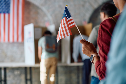 Close up of black woman holding US flag while waiting in a line to vote during elections.