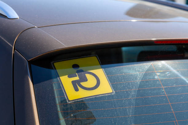 Close-up on a yellow disabled driver sign stuck at the rear window of a car.