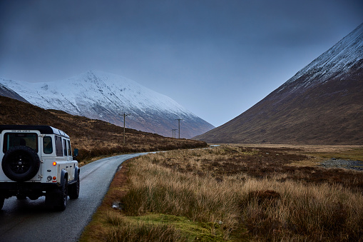 Land Rover Defender 4x4 on the road in Scotland near Elgol during winter time, there is snow on the mountains an the road is leading into the distance.