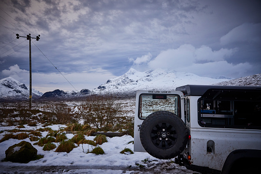 Land rover Defender 4x4 on a with snow covered parking during winter, UK, scotland. In the back you see the mountains of Cuillins, on Isle of Skye.
