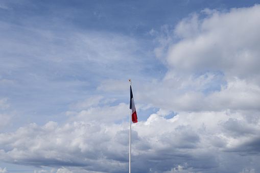 Background image of French National Flag flying in breeze against changing sky - white and storm clouds and blue sky