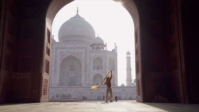 Carefree woman walking and wandering at the famous Taj Mahal at sunrise holding scarf in hands, Agra, India. People travel Asia concept