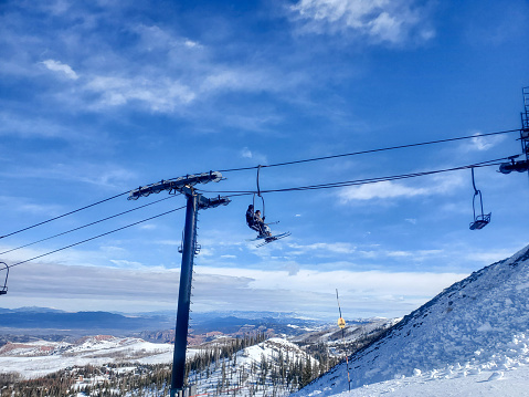 Brian Head, Utah, USA- February 19, 2024: Skiers on a lift with distant valley beyond, Brian Head ski resort, Utah.