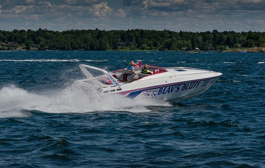 A close up of a speed boat with a black and white hull and a big windshield parked next to a wooden jetty or marina located at the edge of a vast yet shallow river or lake in Poland in summer