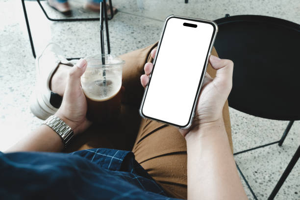 istock A man is sitting in a cafe, holding a blank screen mock-up mobile phone in one hand and a coffee cup in the other. 2042982210