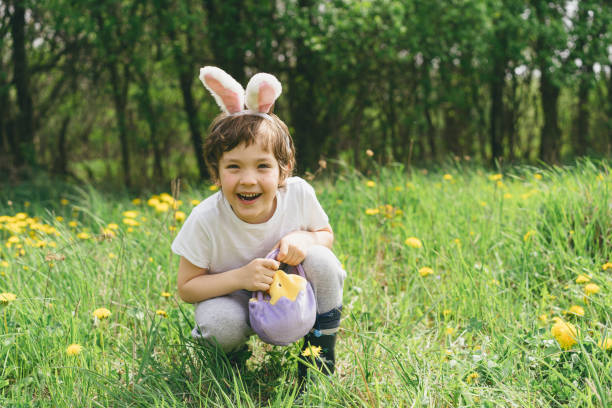 Funny boy with eggs basket and bunny ears on Easter egg hunt in sunny spring garden. Hunting for Easter eggs
