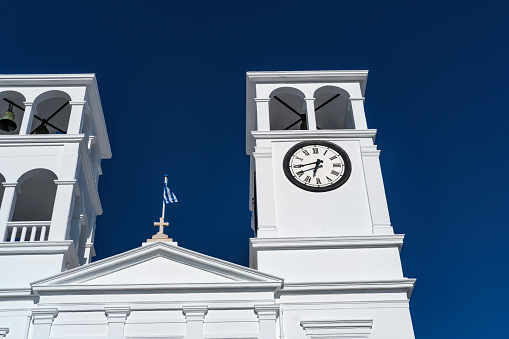 bell and clock tower of typical Greek Orthodox church, whitewashed building in sunlight on blue sky
