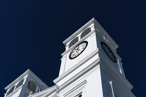 bell and clock tower of typical Greek Orthodox church, whitewashed building in sunlight on blue sky