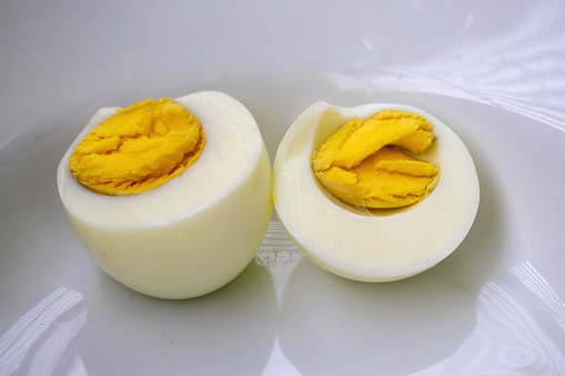 A hard-boiled egg is cut into two pieces. The egg is divided into two equal parts. The yolk of the egg is solid yellow and the white is clear. Nutrition concept.