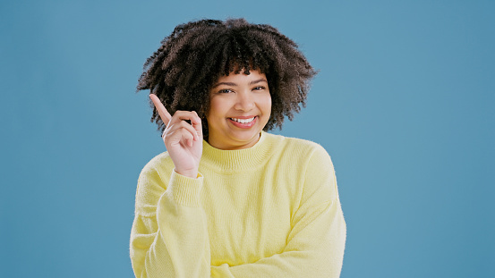 Woman, portrait and smile with pointing in studio with finger for advertising space, promotion presentation or sign up. Person, face and happy with about us and product information on blue background