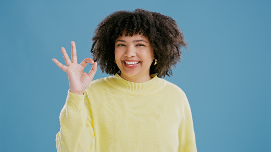 Happy, woman and sign ok with hand in portrait on studio, blue background and feedback mockup. Opinion, review and emoji of girl with gesture for okay, thanks and icon of agreement with fashion