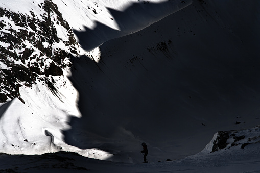 Silhouette of a child on skis in the shadow of a threatening mountain